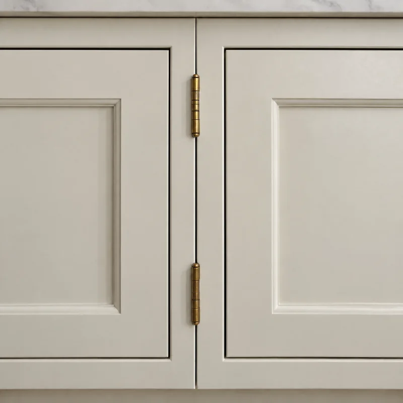 Close-up of cream-painted inset cabinet doors sitting flush in their face frame with narrow even reveals and small brass butt hinges