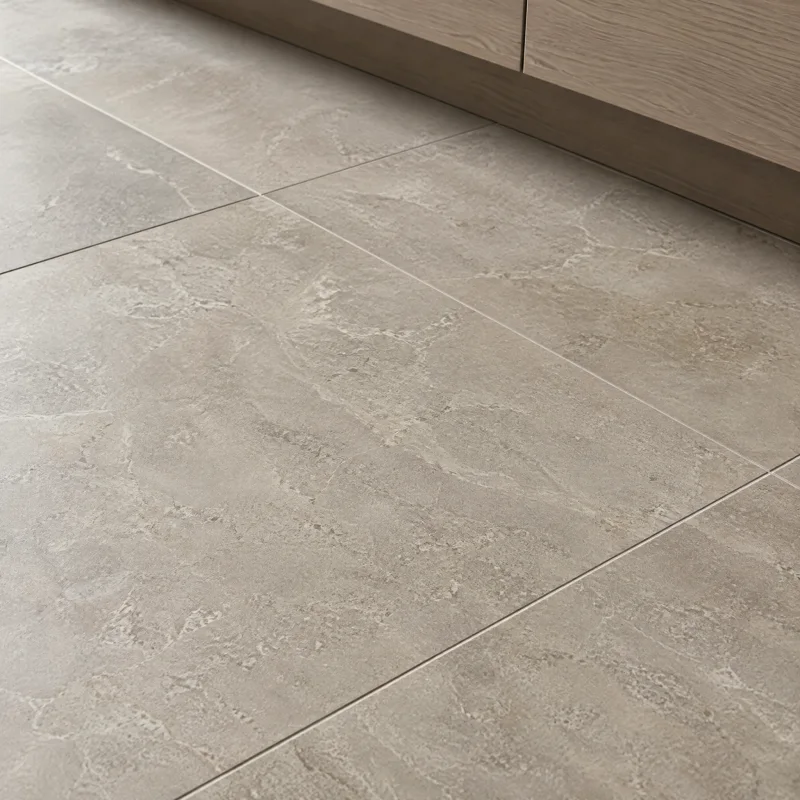 Close-up of large-format matte porcelain floor tile in a warm greige stone look with narrow tight grout lines