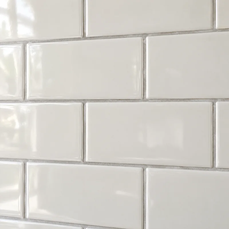 Close-up of glossy warm-white ceramic subway tile with pale grey grout in a running bond