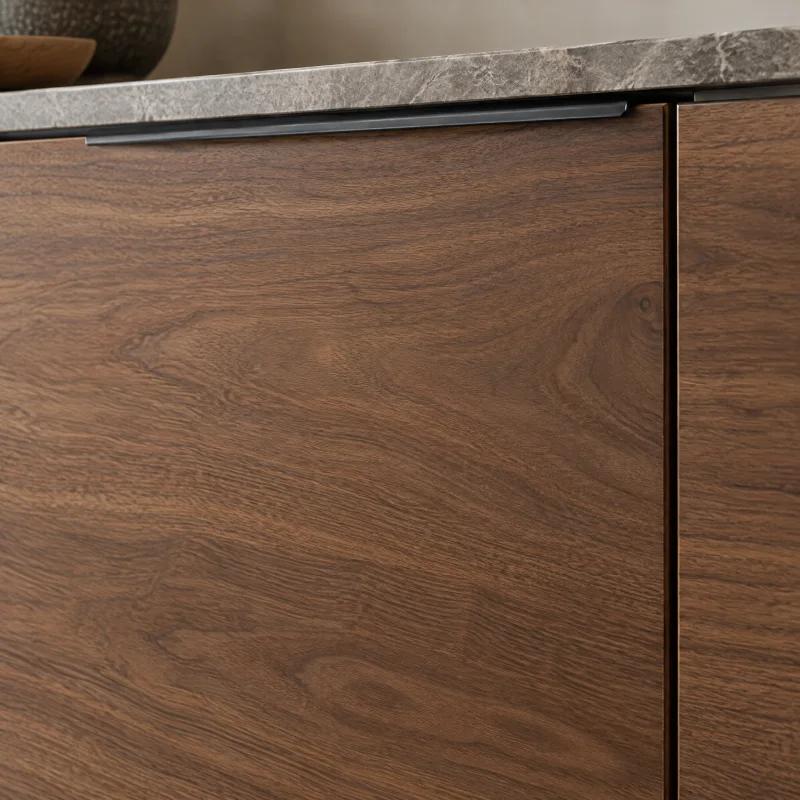 Close-up of a flat walnut cabinet door with a rich brown flowing grain, satin finish, and a slim matte black edge pull